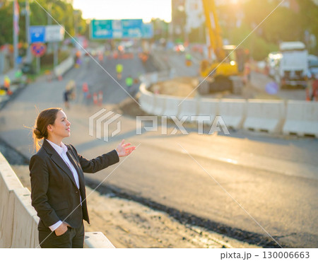AI generated A professional civil engineer stands at the frame edge gesturing toward an active road construction site. The infrastructure development scene showcases urban planning, engineering 130006663