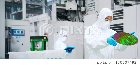 半導体工場でシリコンウエハーを検査する防護服を着た男性作業員 半導体工場でシリコンウエハーを検査する防護服を着た男性作業員 130007492