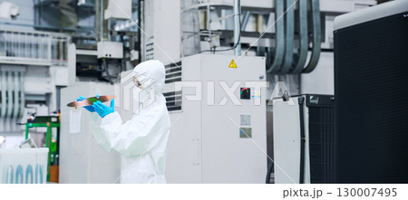 半導体工場でシリコンウエハーを検査する防塵服を着た女性作業員 130007495