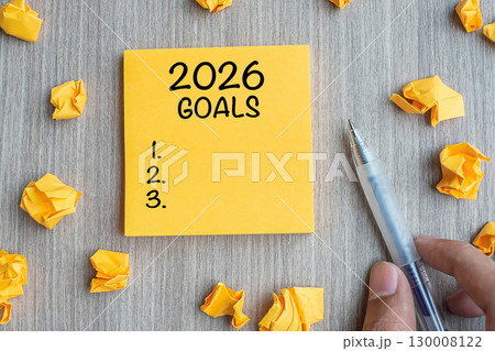 2026 Goal word on yellow note with Businessman holding pen and crumbled paper on wooden table background. New Year New Start, Resolutions, Strategy, mission concept 130008122