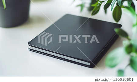 A black tablet sits on a table next to a potted plant 130010601