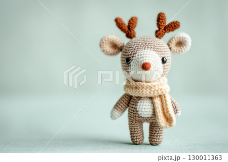 Adorable knitted reindeer toy wearing a cozy scarf, showcasing intricate craftsmanship and soft textures against a gentle pastel background 130011363