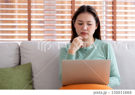 Young asian business woman working with laptop while thoughtful sitting on sofa in home office. Young asian business woman working with laptop while thoughtful sitting on sofa in home office. 130011668
