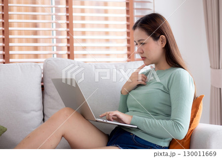 Young asian business woman working with laptop while thoughtful sitting on sofa in home office. 130011669