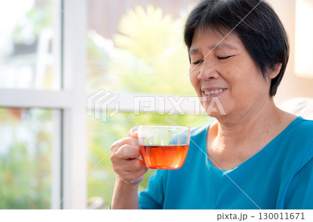 Senior asian woman enjoying drinking tea sitting on sofa with satisfied in living room at home. 130011671