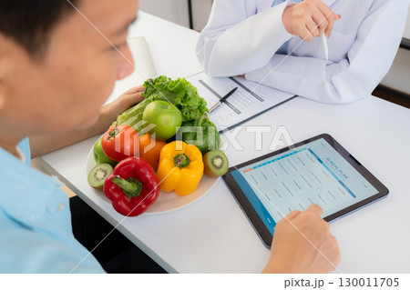 Asian nutritionist using tablet to explaining personalized meal plan with AI to patient. 130011705