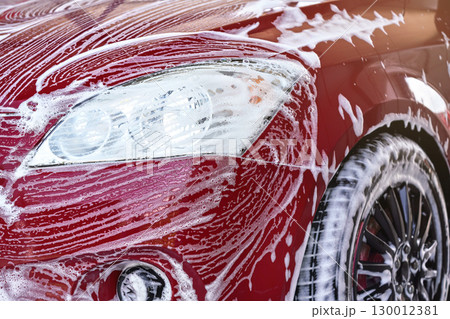 Detail on red car front light washed in carwash, white soap strokes on surface 130012381