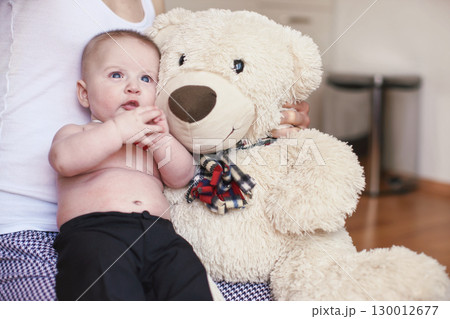 Four months old baby boy sitting on her mother knees, large plush teddy bear next to him Four months old baby boy sitting on her mother knees, large plush teddy bear next to him 130012677