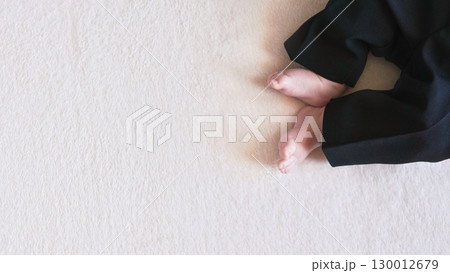 Baby boy legs in black trousers, on white towel cloth, view from above, wide banner with space for text on left side. 130012679