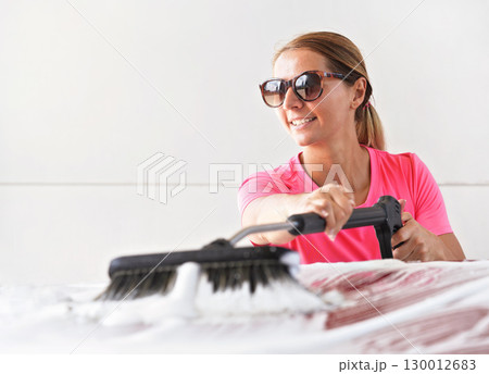 Young woman wearing pink t shirt and sunglasses cleaning her car in self service carwash 130012683