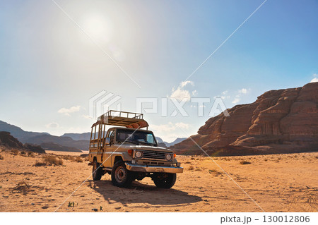 4WD off road vehicle parked in desert, backlight sun shines on mountains background - typical scenery of Wadi Rum, Jordan 4WD off road vehicle parked in desert, backlight sun shines on mountains background - typical scenery of Wadi Rum, Jordan 130012806