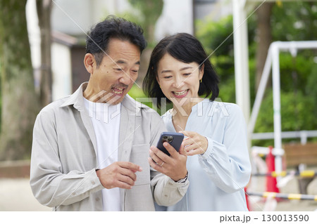 中年の夫婦 スマートフォンを使う 屋外 中年の夫婦 スマートフォンを使う 屋外 130013590