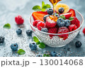 Chia pudding with fresh berries, banana slices, and honey drizzle, served in a glass bowl with mint leaves. 130014068