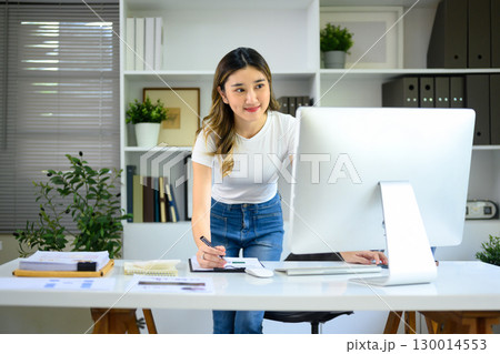 Young entrepreneur working at desktop computer and taking notes in modern office. 130014553