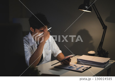 Stressed businessman working late at night, holding tablet and rubbing eyes from fatigue Stressed businessman working late at night, holding tablet and rubbing eyes from fatigue 130014585