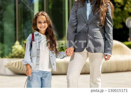 Mother and daughter posing happily near sleek urban bench and glass building 130015171