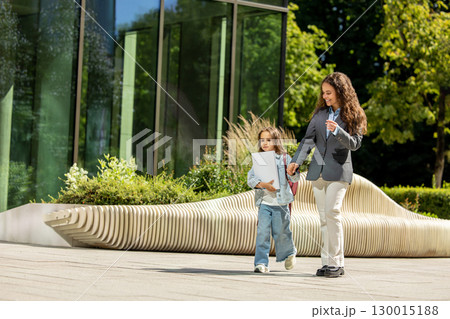 Woman in blazer with daughter walking in city street 130015188