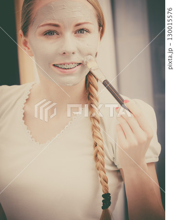 Woman applying with brush clay mud mask to her face 130015576