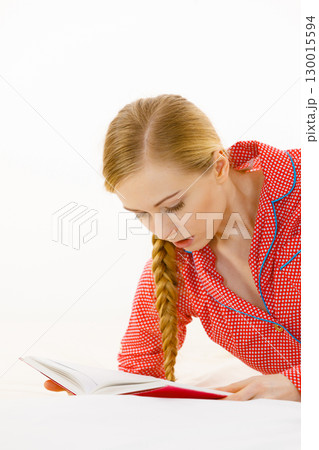 Woman relaxing in bed reading book 130015594