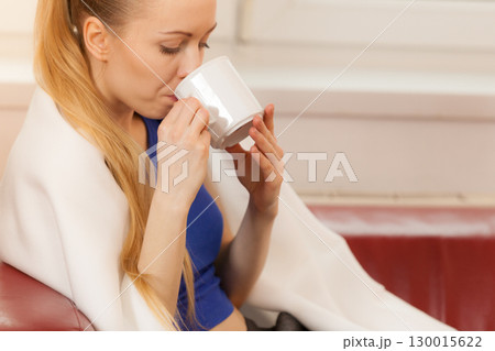 Woman lying on sofa under blanket drinking tea Woman lying on sofa under blanket drinking tea 130015622