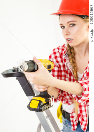 Woman using drill on ladder 130015667