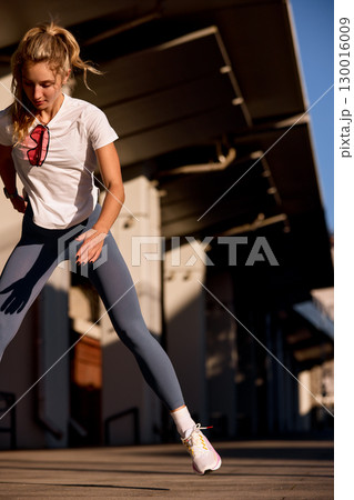 Young woman performing an outdoor workout in early morning sunlight 130016009