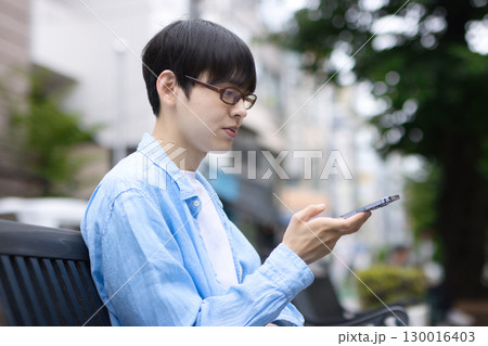 街中のベンチに座ってスマホを見る若い男性 街中のベンチに座ってスマホを見る若い男性 130016403