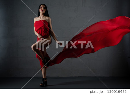 Captivating woman in red lingerie draped with flowing cloth in a dramatic pose 130016483