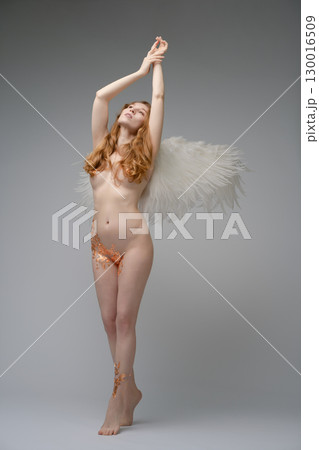 Red naked woman with angel wings showcases body art in a studio setting Red naked woman with angel wings showcases body art in a studio setting 130016509
