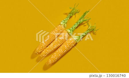 Three braided corn cobs on yellow background Three braided corn cobs on yellow background 130016740