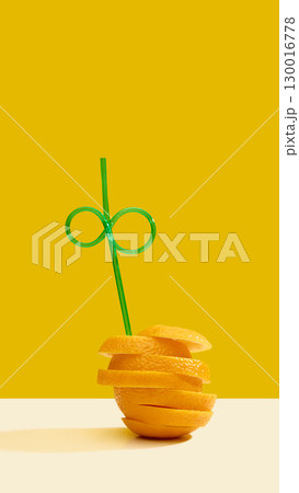 Orange slices stacked with green straw on yellow background 130016778