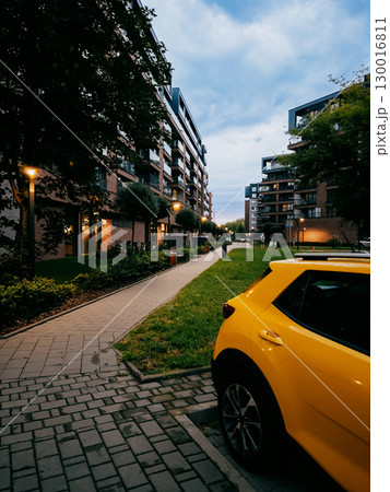Yellow car parked on paved street, surrounded by modern residential buildings at dusk, creating tranquil and serene urban atmosphere in peaceful neighborhood. Yellow car parked in residential area Yellow car parked on paved street, surrounded by modern residential buildings at dusk, creating tranquil and serene urban atmosphere in peaceful neighborhood. Yellow car parked in residential area 130016811