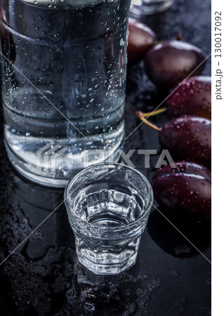 Distilled alcohol and plums on black table. Plum brandy shot. 130017092