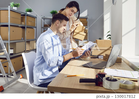 Young cheerful colleagues working at workplace in storeroom checking stock and inventory. Young cheerful colleagues working at workplace in storeroom checking stock and inventory. 130017812