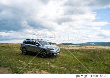 Silver SUV on Grassy Hill with Cloudy Sky 130018570