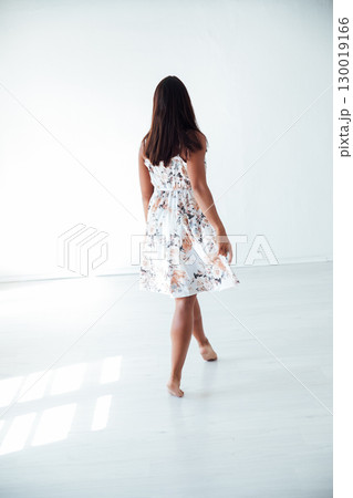 Tanned brunette woman in summer dress with flowers in white room Tanned brunette woman in summer dress with flowers in white room 130019166