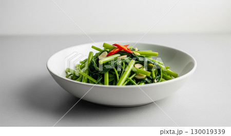 A Minimalist Bowl of Stir Fried Morning Glory on a Gray Background 130019339