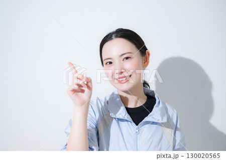 スポーツウェアで応援する女性のカメラ目線　笑顔のクローズアップ　指差しのポイントやno1 130020565