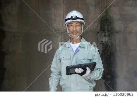 カメラ目線で笑顔の作業服姿のタブレットを持った60代の男性 カメラ目線で笑顔の作業服姿のタブレットを持った60代の男性 130020962