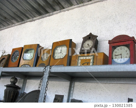 A row of vintage wooden clocks on a metal shelf, showcasing diverse designs and aged faces, reflecting the passage of time in a nostalgic antique setting A row of vintage wooden clocks on a metal shelf, showcasing diverse designs and aged faces, reflecting the passage of time in a nostalgic antique setting 130021385