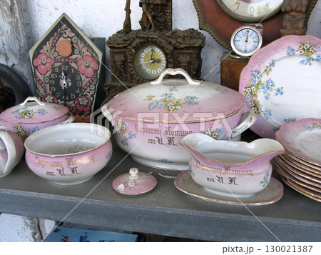 A set of vintage pink porcelain dishes with floral designs and lids, displayed alongside clocks, reflecting elegant tableware from a bygone era A set of vintage pink porcelain dishes with floral designs and lids, displayed alongside clocks, reflecting elegant tableware from a bygone era 130021387