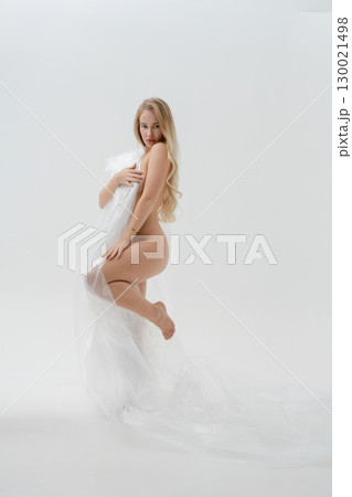 Elegant blonde woman posing in a beauty studio with soft white drapery 130021498