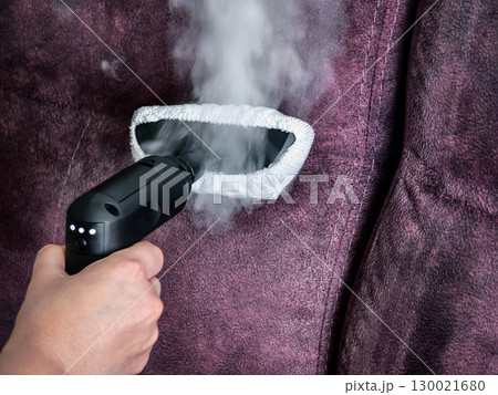 Steam cleaning a purple upholstered couch with a handheld device while removing dirt and allergens in a living room setting 130021680