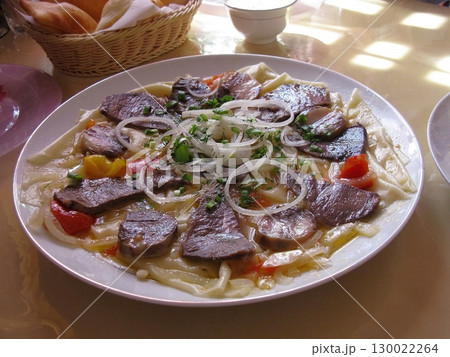 Large Plate of Pasta with Sliced Meat, Onions, and Peppers in a Dining Setup 130022264