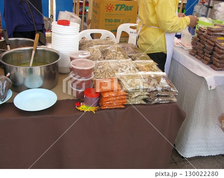 Vibrant Market Stall Offering Spices, Snacks, and a Pot of Soup with Stacked Bowls Nearby 130022280