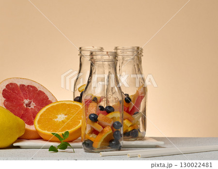 Empty glass bottles filled with citrus slices and blueberries, arranged on a white board. A half grapefruit, a half orange, a whole lemon 130022481