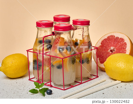 Glass bottles with red lids, filled with detox water infused with citrus slices and blueberries, in a red wire holder. A whole lemon, a half grapefruit Glass bottles with red lids, filled with detox water infused with citrus slices and blueberries, in a red wire holder. A whole lemon, a half grapefruit 130022482