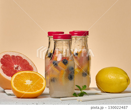 Glass bottles filled with detox water infused with citrus slices and blueberries. A half grapefruit, orange, whole lemon, and paper straws 130022487