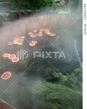 Steamy Hot Tub with Floating Citrus Slices and Pine Branches in a Relaxing Setting 130022799