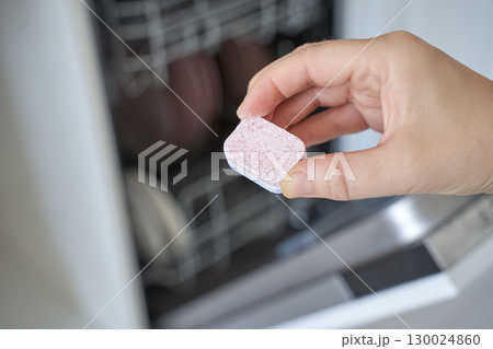 Hand holding dishwasher tablet in front of open dishwasher with clean dishes Hand holding dishwasher tablet in front of open dishwasher with clean dishes 130024860